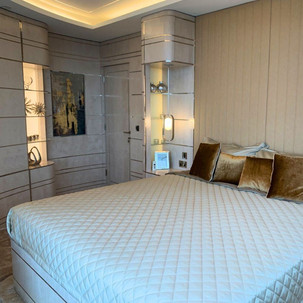 Elegant bedroom with curved storage units and gold velvet pillows in Albert Embankment penthouse.
