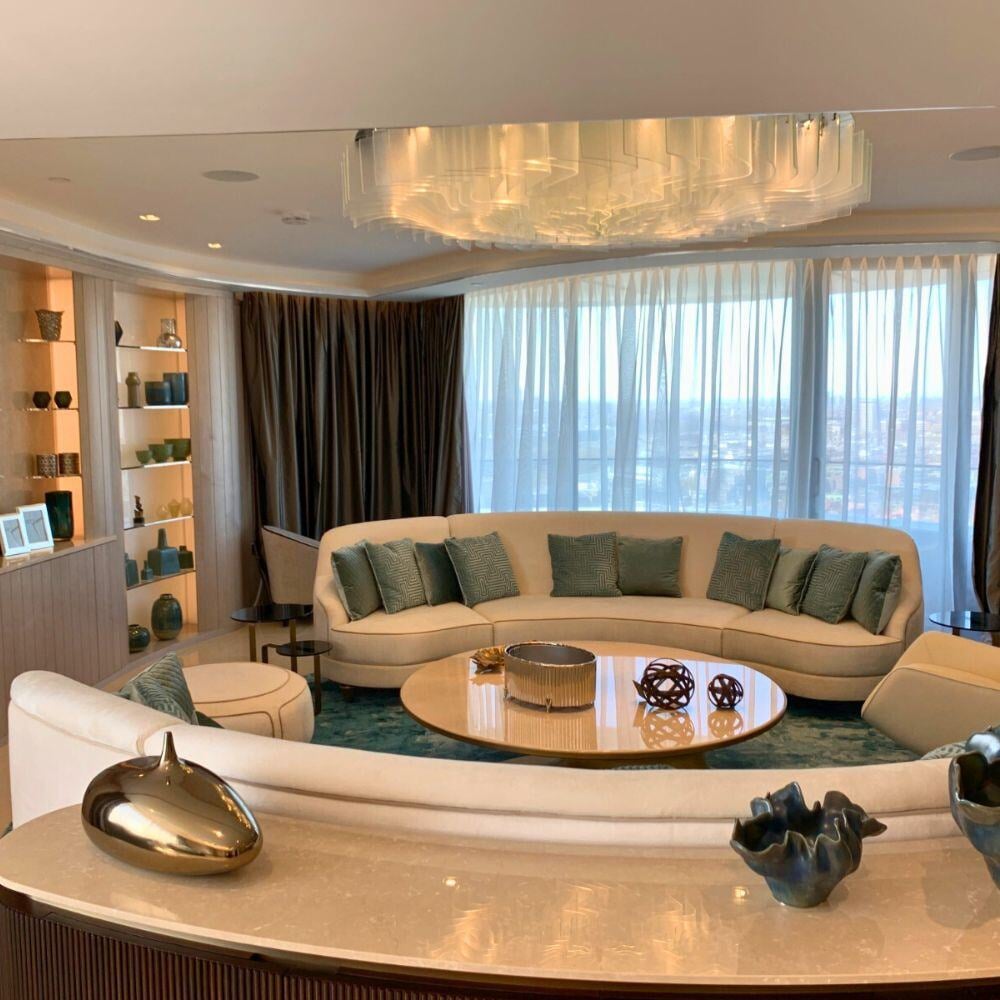 Wide-angle shot of curved sofa in luxury penthouse living room with teal and gold accents.