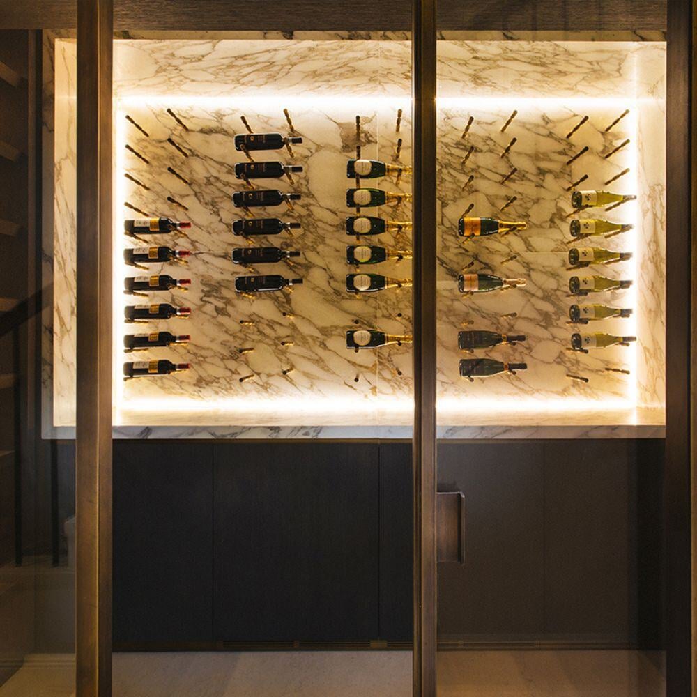 Luxury marble wine cellar with backlit champagne display and bespoke bronze framing in Belgravia, Central London.