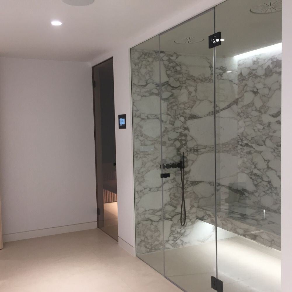 Spa-inspired marble steam room with glass enclosure and built-in bench in Belgravia home renovation.