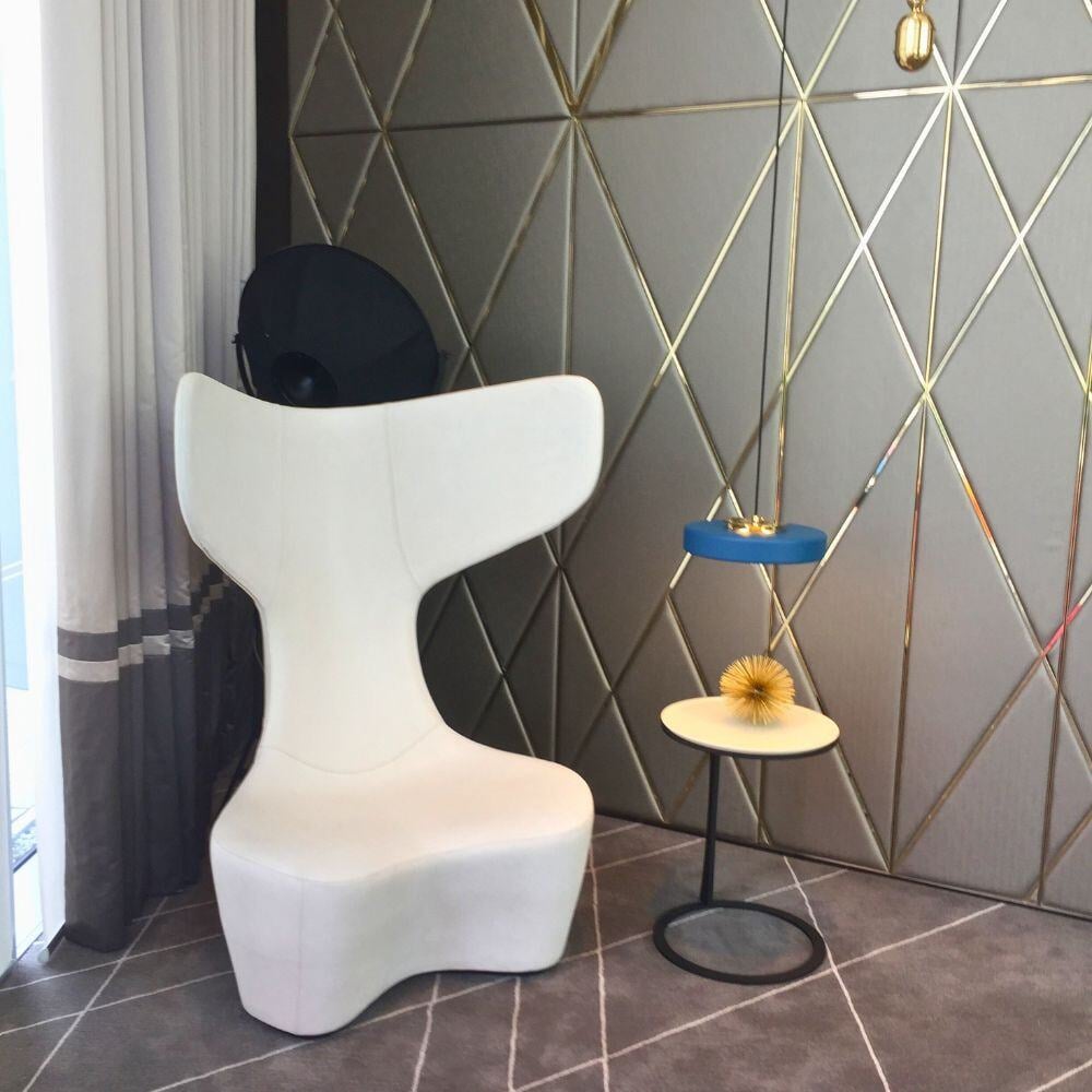 Artistic waiting corner with sculptural chair, lighting and brass-accented panel walls.
