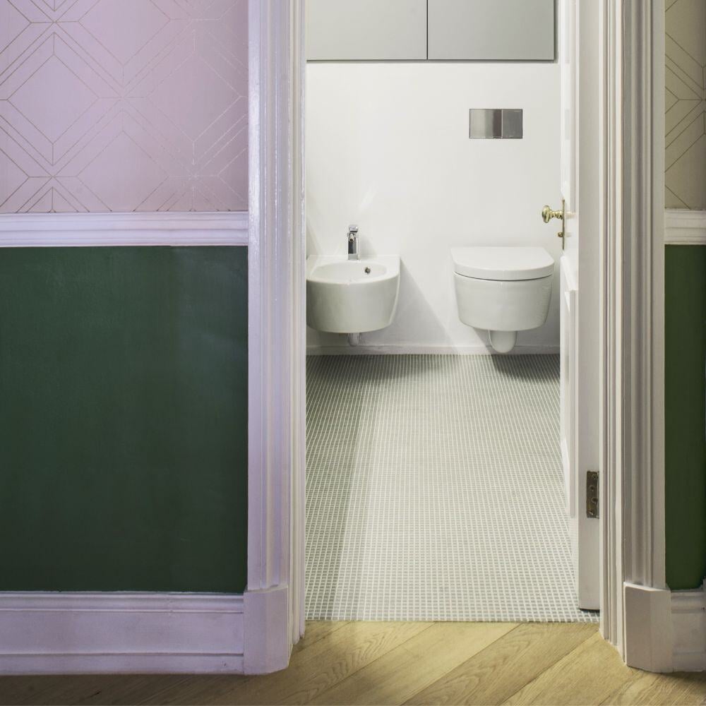Modern guest bathroom with white mosaic tiles and wall-mounted fixtures, viewed from a green panelled hallway.