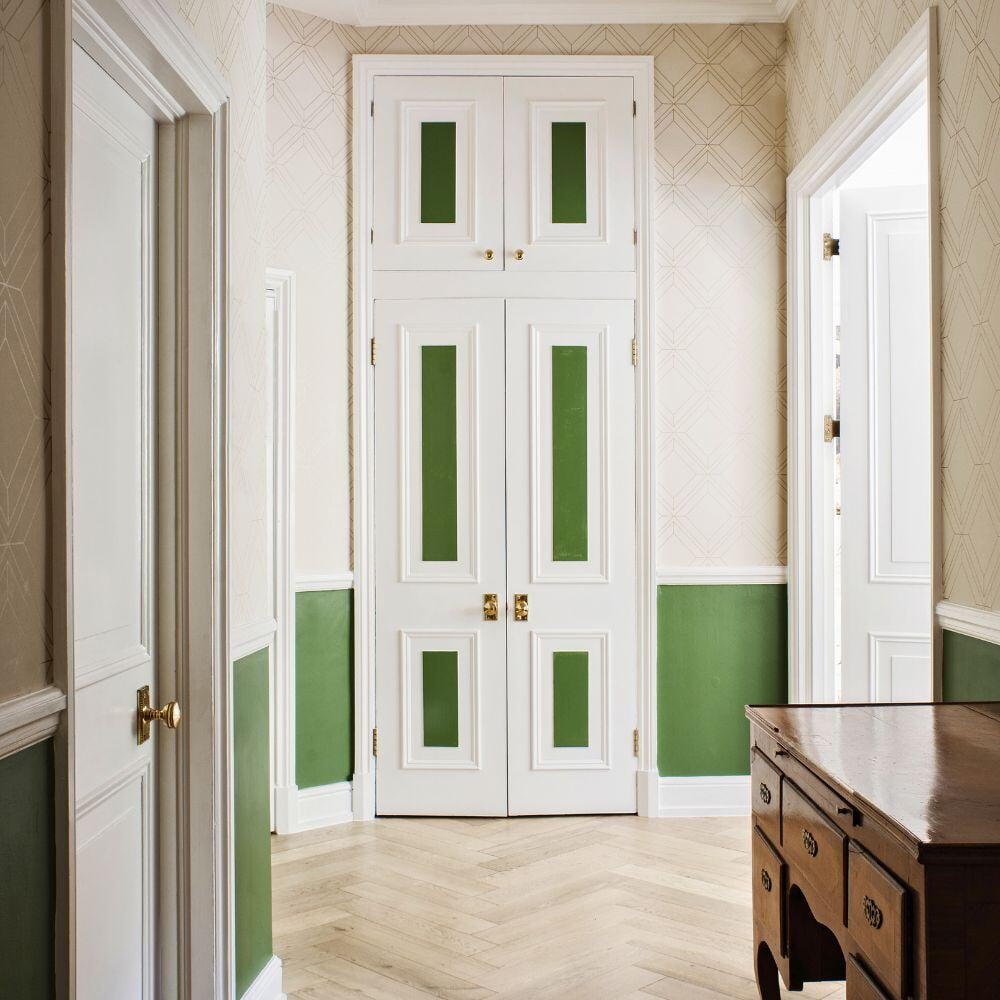 Elegant hallway with herringbone wood flooring and classic white cabinetry with green accents in London apartment.