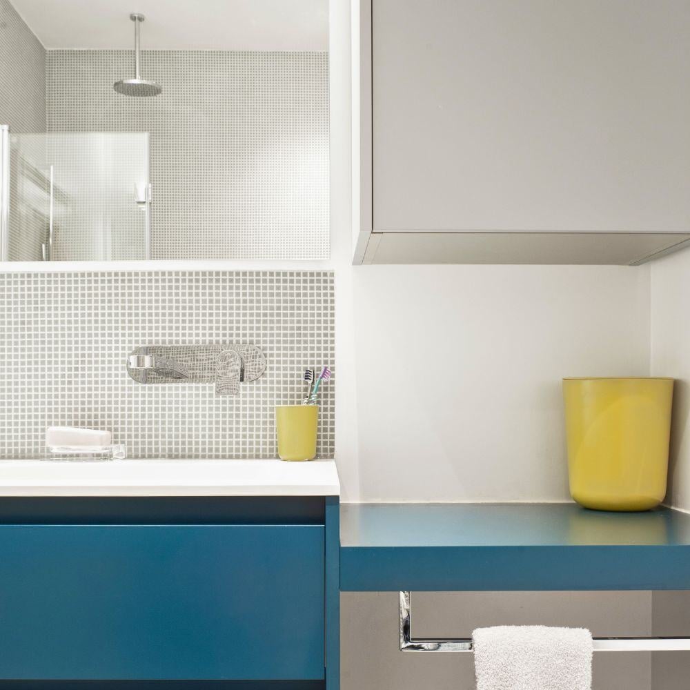 Stylish bathroom with blue vanity, white mosaic tiles, and yellow accents in contemporary interior project.