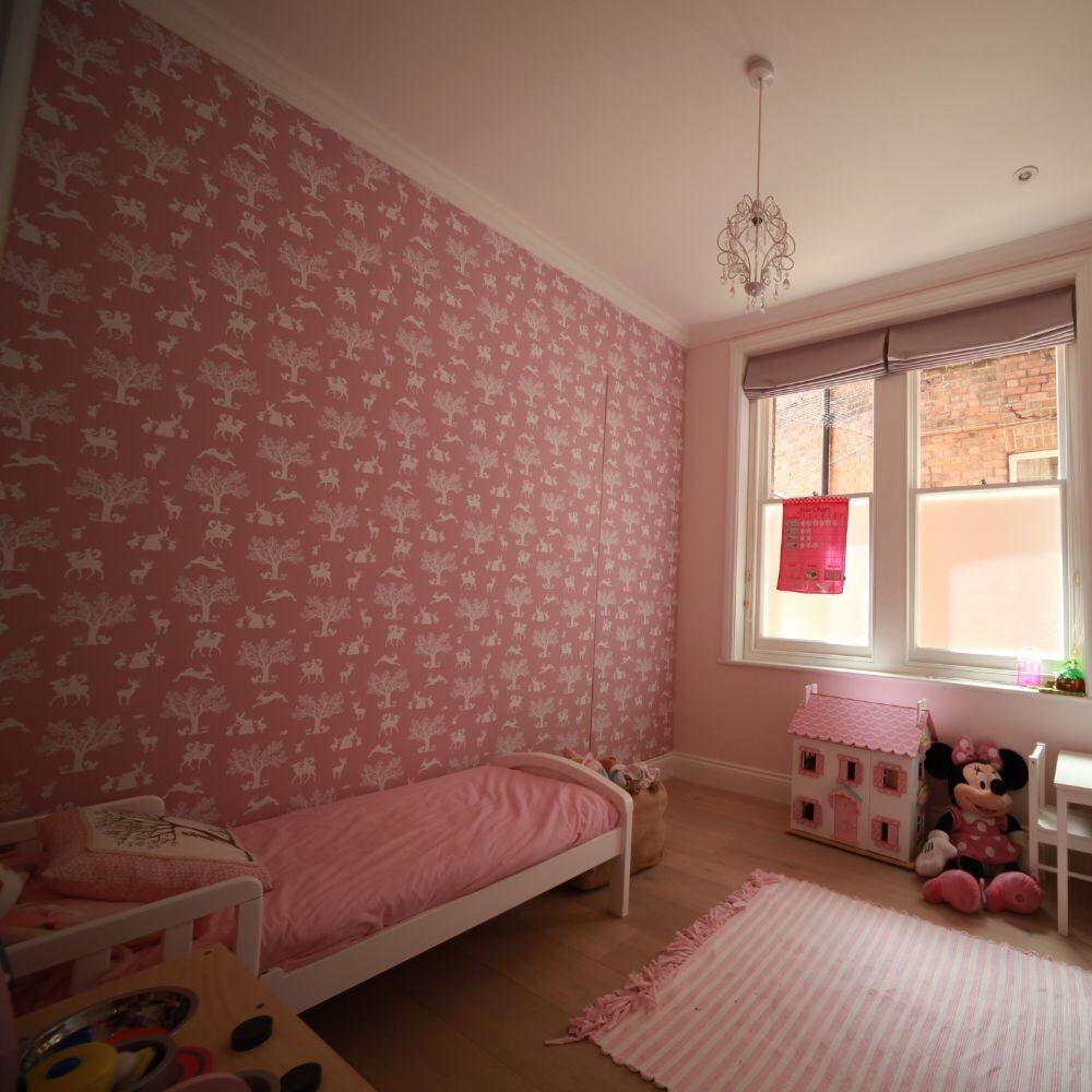 Children bedroom with playful pink wallpaper and soft furnishing details.