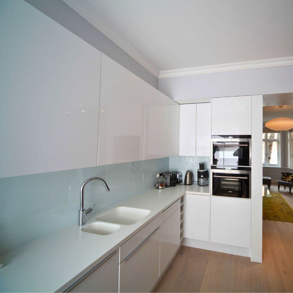 Angle view of a sleek modern white kitchen with integrated appliances and minimalist design.