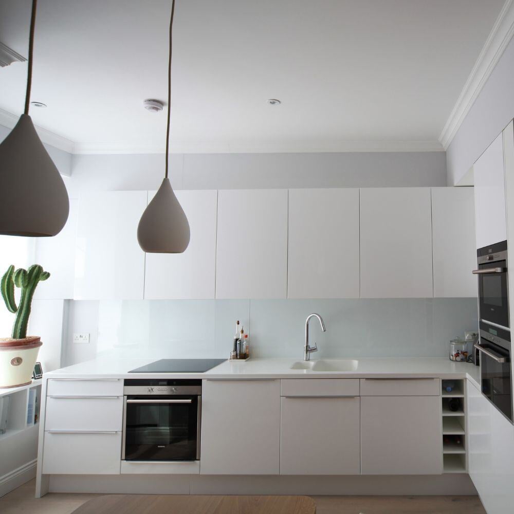 Front view of a clean and contemporary white kitchen with high gloss cabinets and integrated sink.