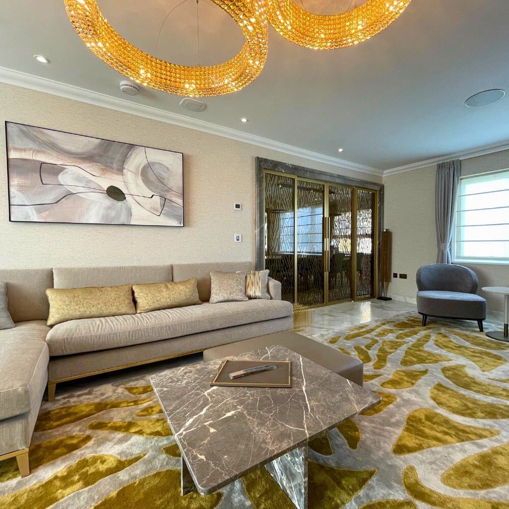 Elegant living room with gold chandelier, green abstract rug, and a marble coffee table centerpiece.