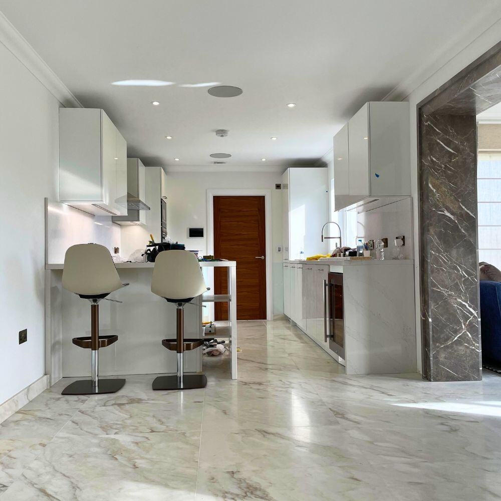 Contemporary open-plan kitchen with polished marble floors, white cabinetry, and breakfast bar seating.