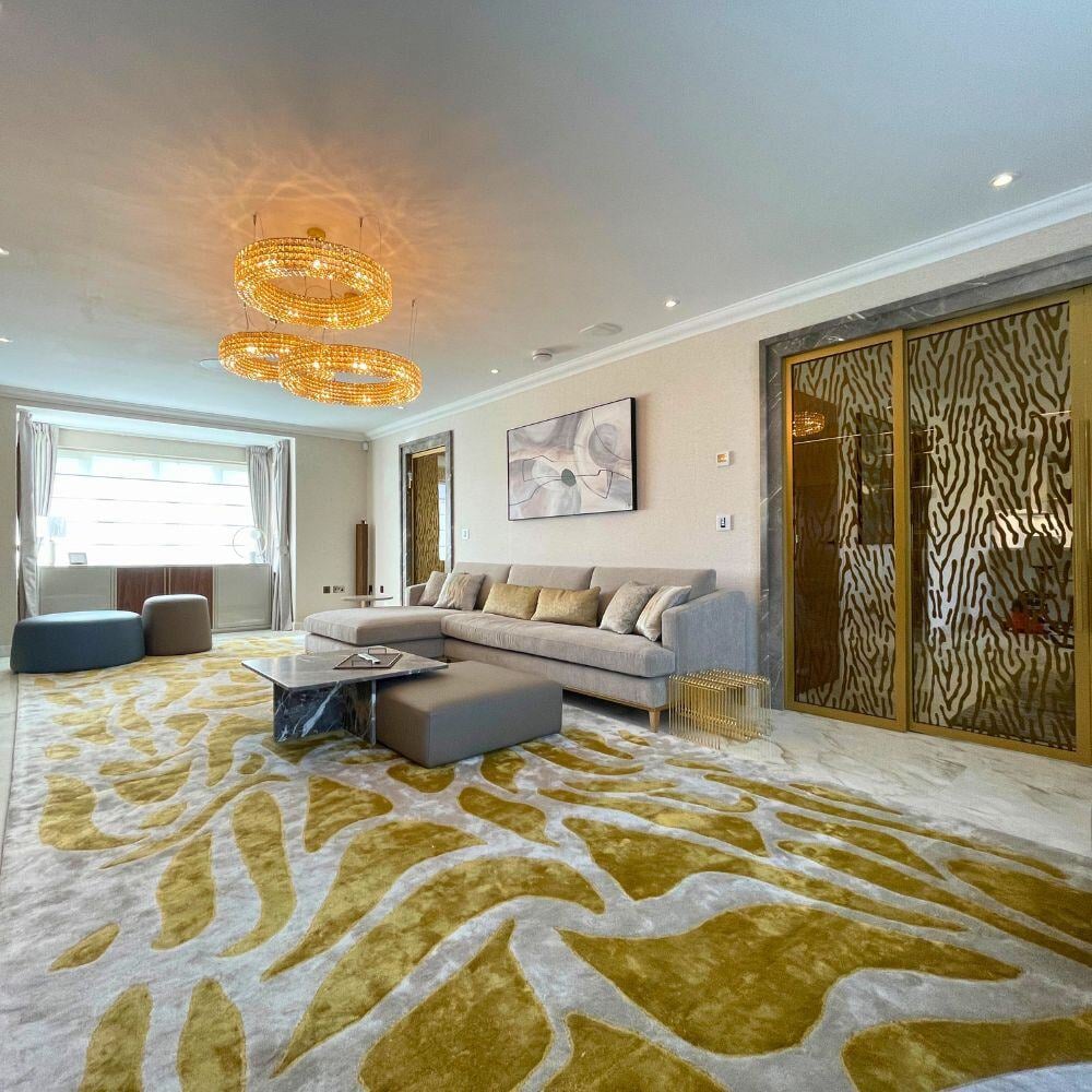 Modern living room featuring curved sofa, bold carpet design, marble floor, and glass panel doors.
