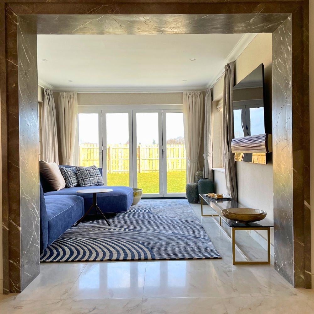 Contemporary living room with a marble-framed entrance, blue corner sofa, and large glass doors overlooking the garden.