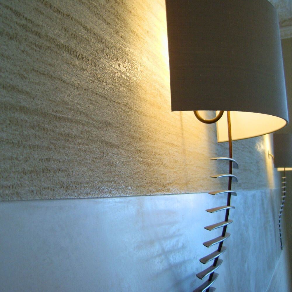 Artistic wall light fixture casting ambient glow on tactile textured wall surface.
